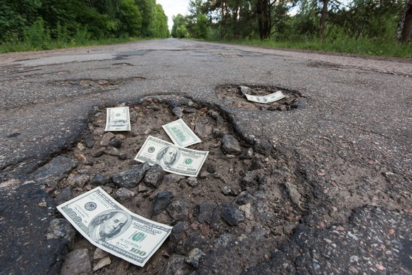 Hundred-dollar bills strewn across potholes in a long, straight road.