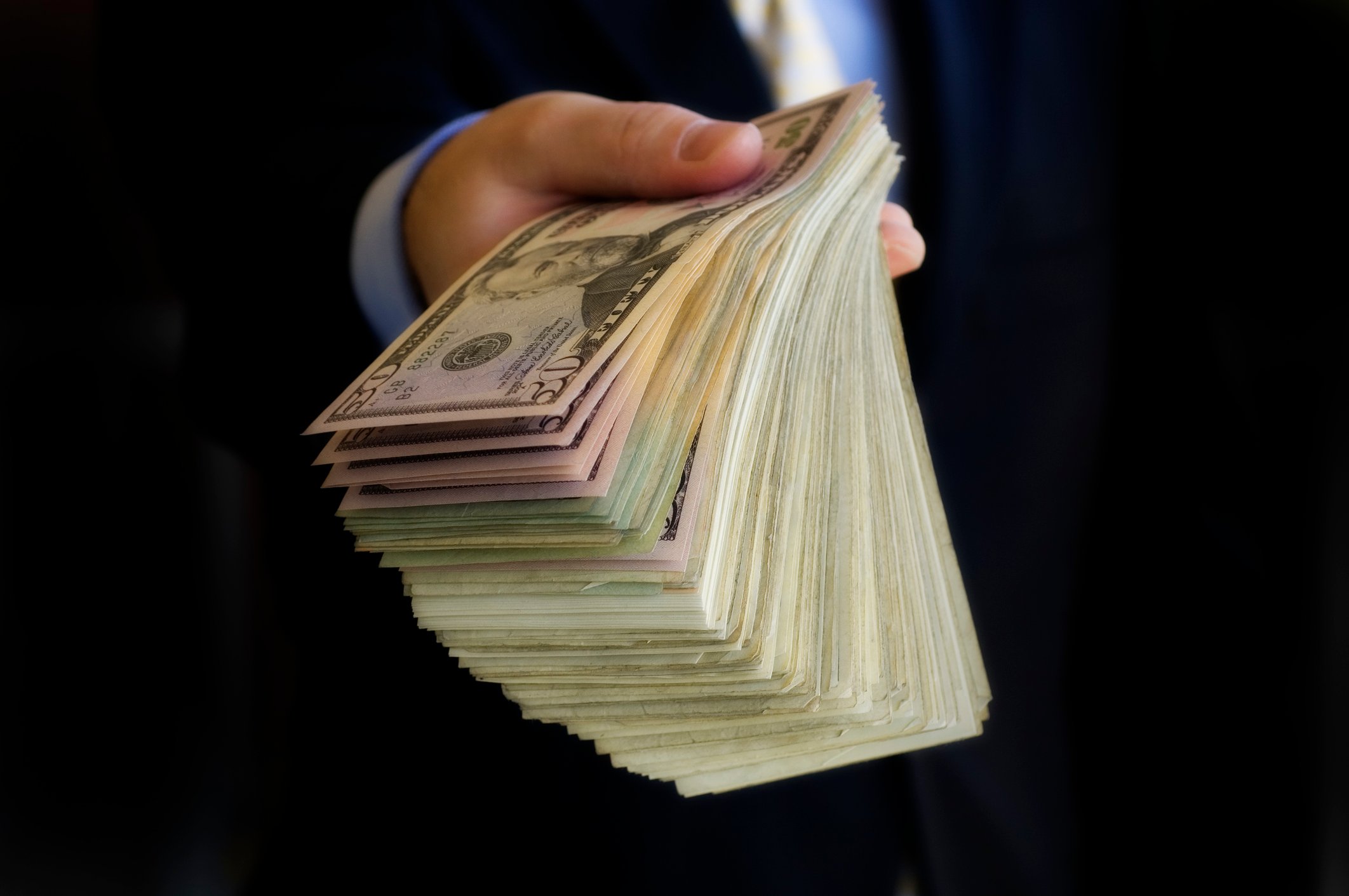 An investor's hand holds out a wad of cash.