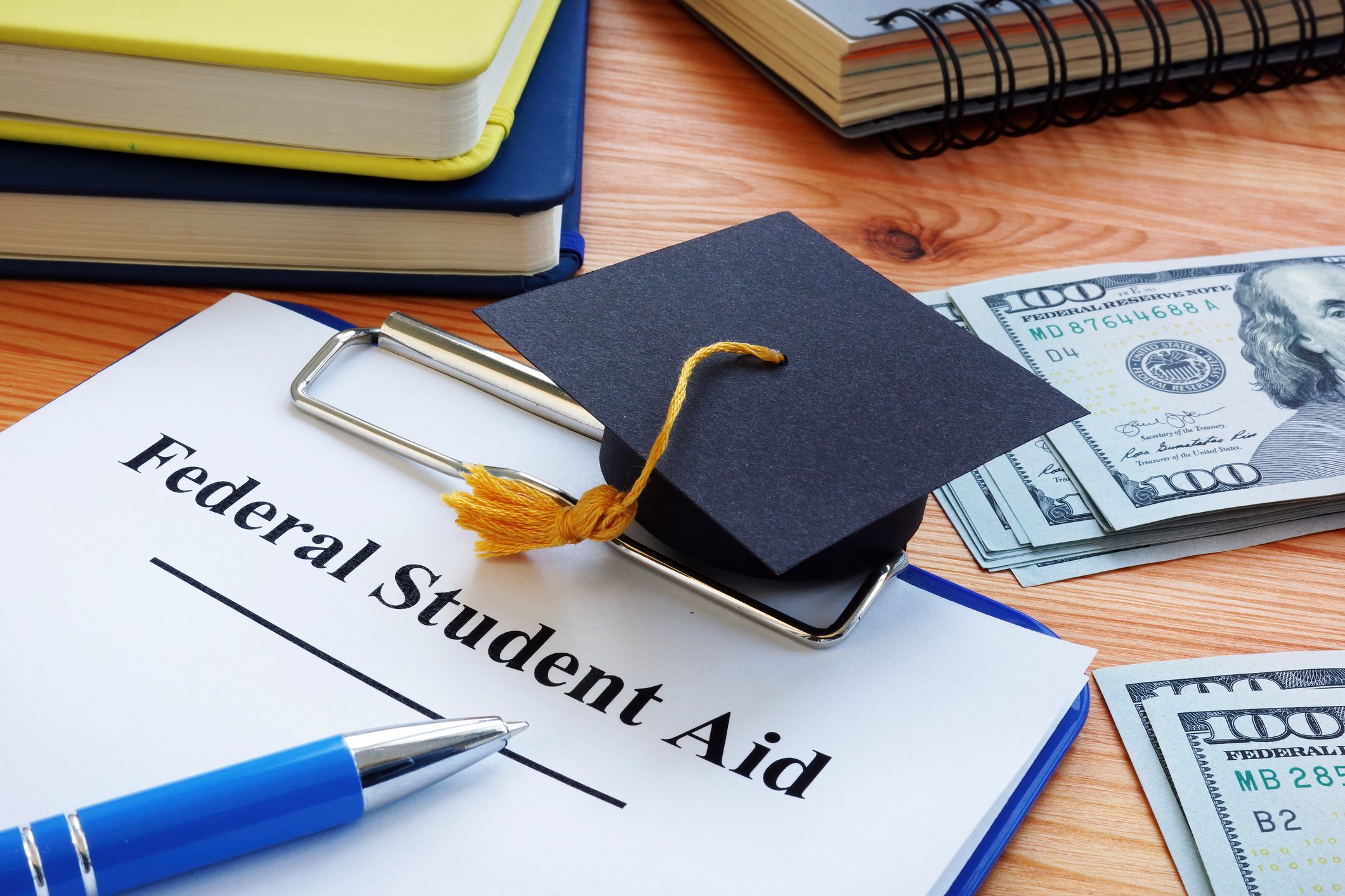 A table with notebooks, money, a cap with tassel, and a clipboard with a document that reads "Federal Student Aid"