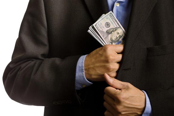 A businessman puts a thick stack of hundred-dollar bills in his jacket's inside pocket.