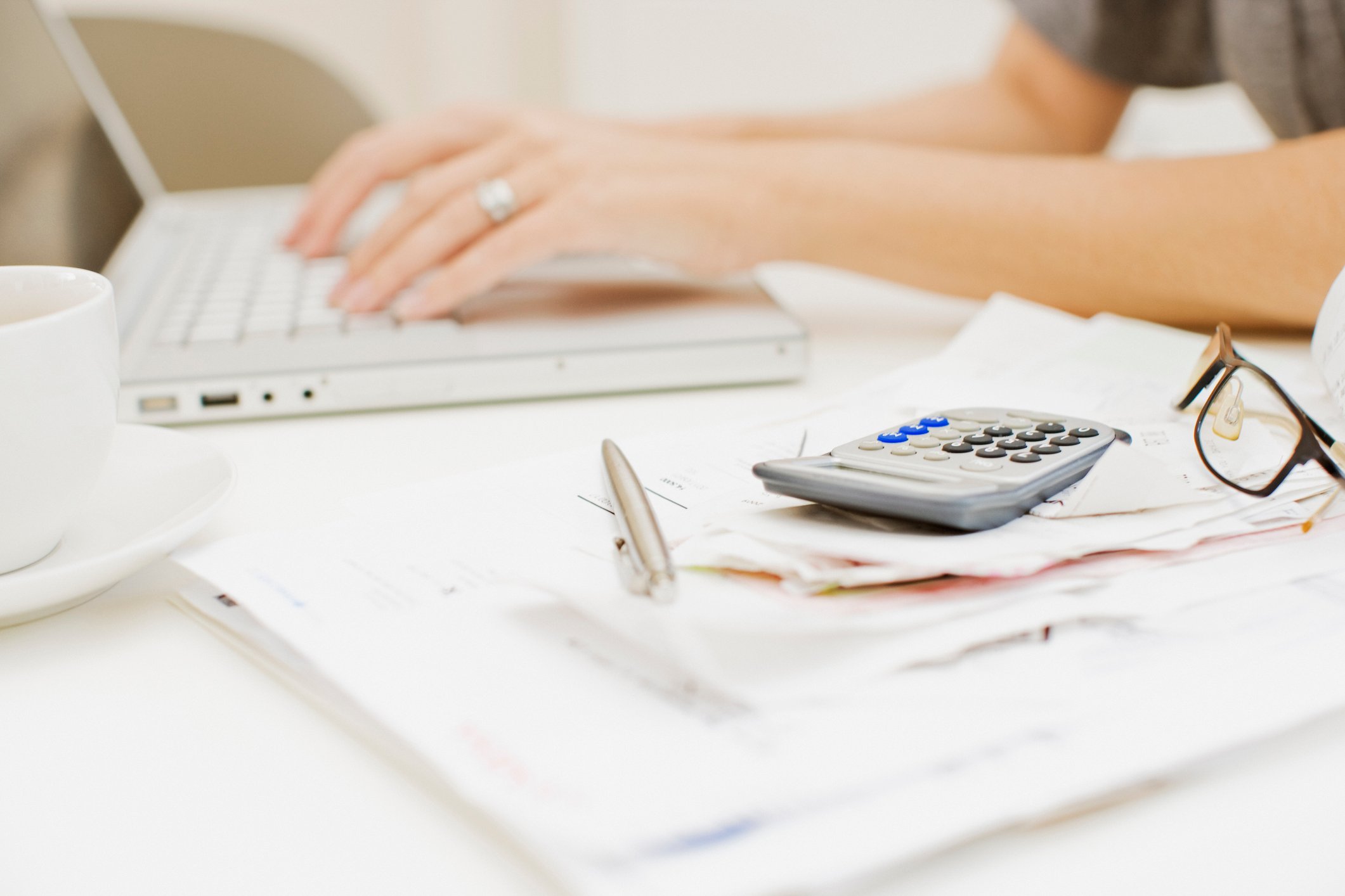 A woman working on her computer with a calculator and pen visible