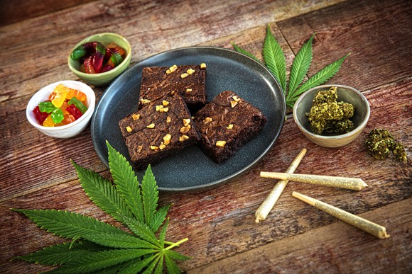 Marijuana leaves, joints, flower, and edibles on a wood table