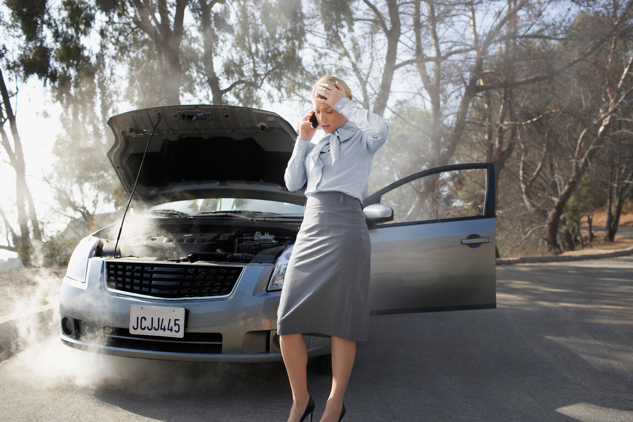 Woman on cell phone standing in front of a broken-down car.