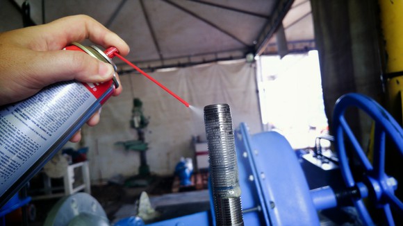 Person spraying degreaser fluid on a metal part of a machine