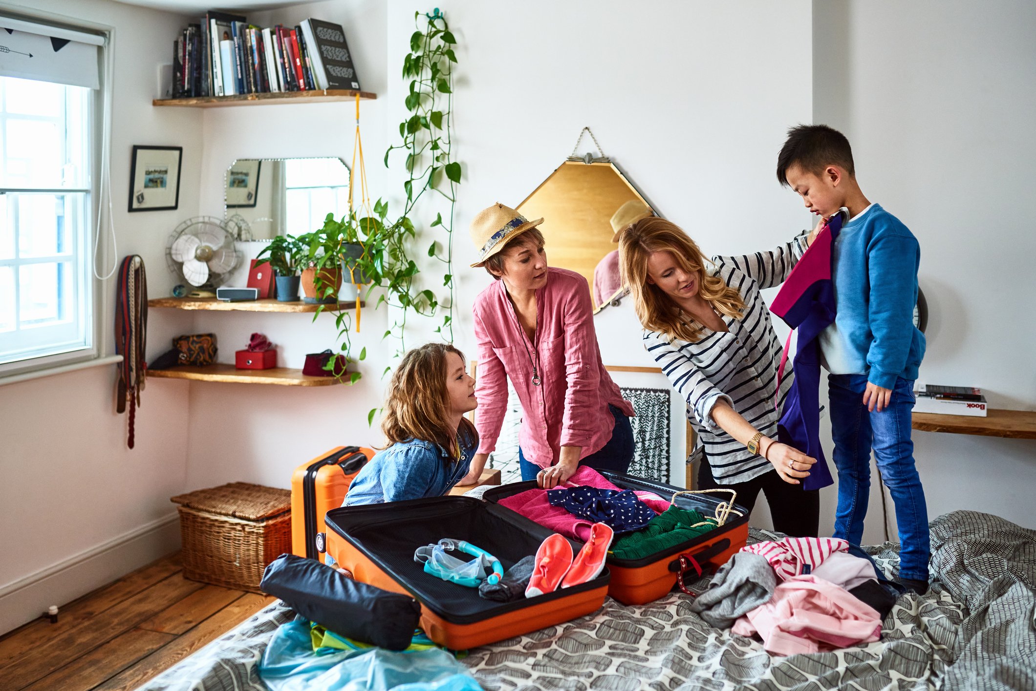 Two children and two adults unpacking a suitcase in a bedroom.