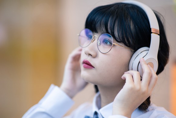 A young girl listens to big white noise cancelling headphones. 