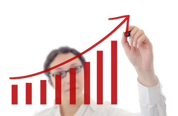 A woman drawing an arrow that is steadily rising on a white board with a red marker.