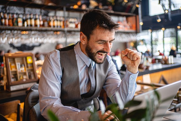 male investor looking excitedly at computer screen and cheering for joy