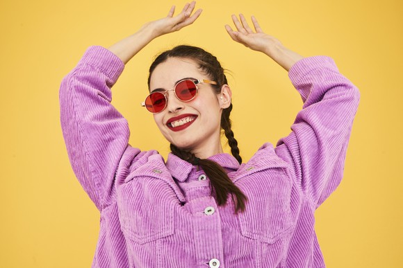 Person in purple jacket and sunglasses smiling and dancing.