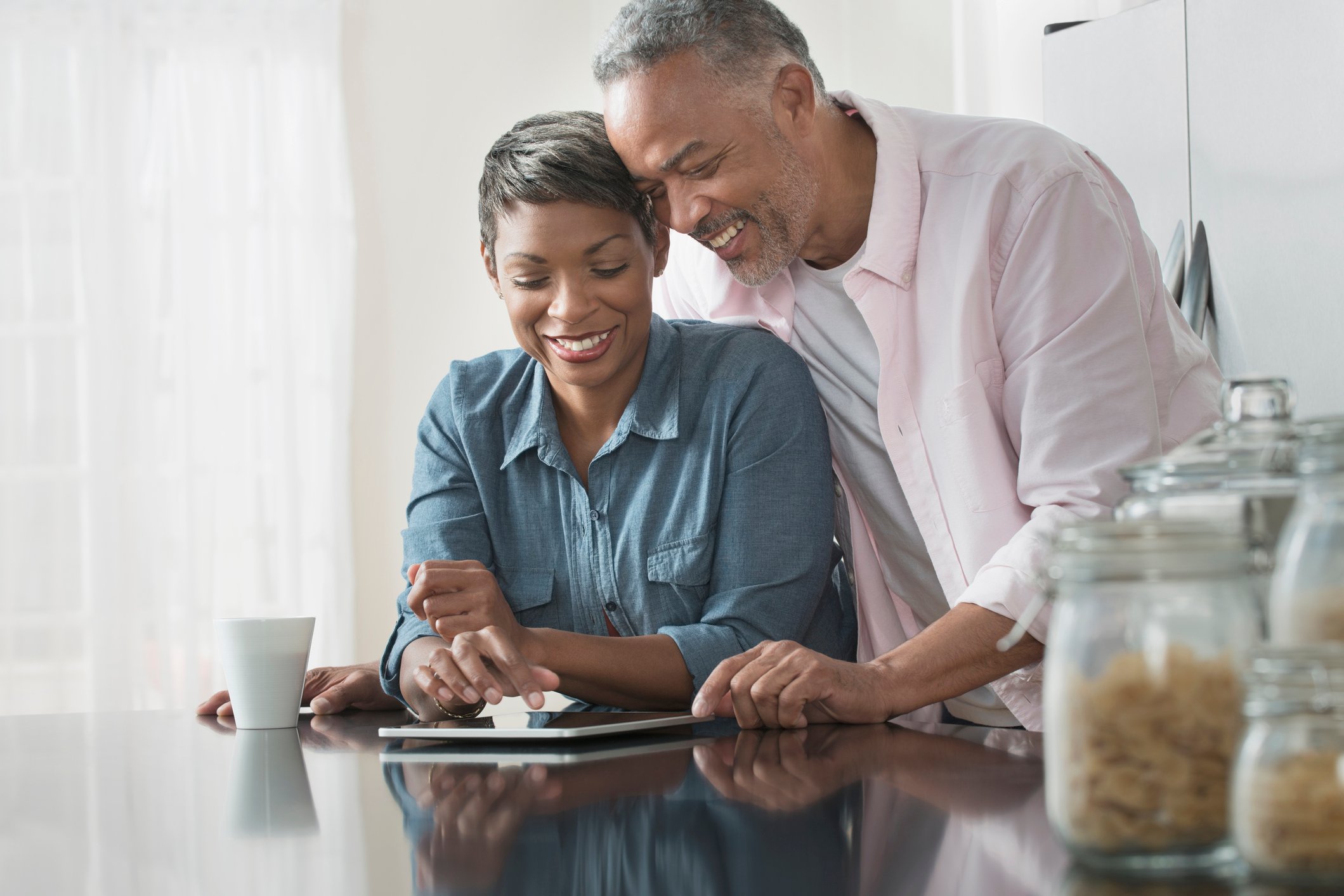 Smiling couple at kitchen counter reviewing a tablet