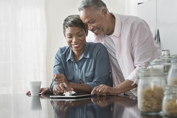 Smiling couple at kitchen counter reviewing a tablet