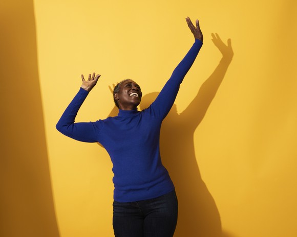 Happy person dancing against a bright yellow background.