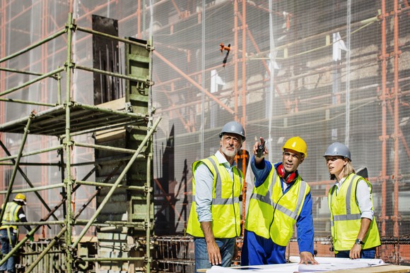 A group of workers in hard hats discussing a site plan at a construction site. 