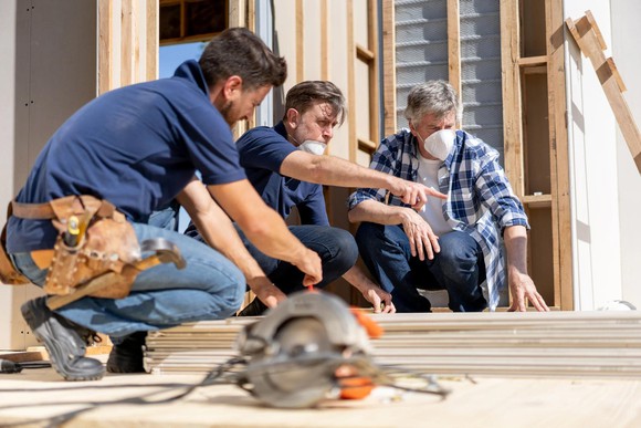 Three workers at a home construction site, with tools and a rotary saw.