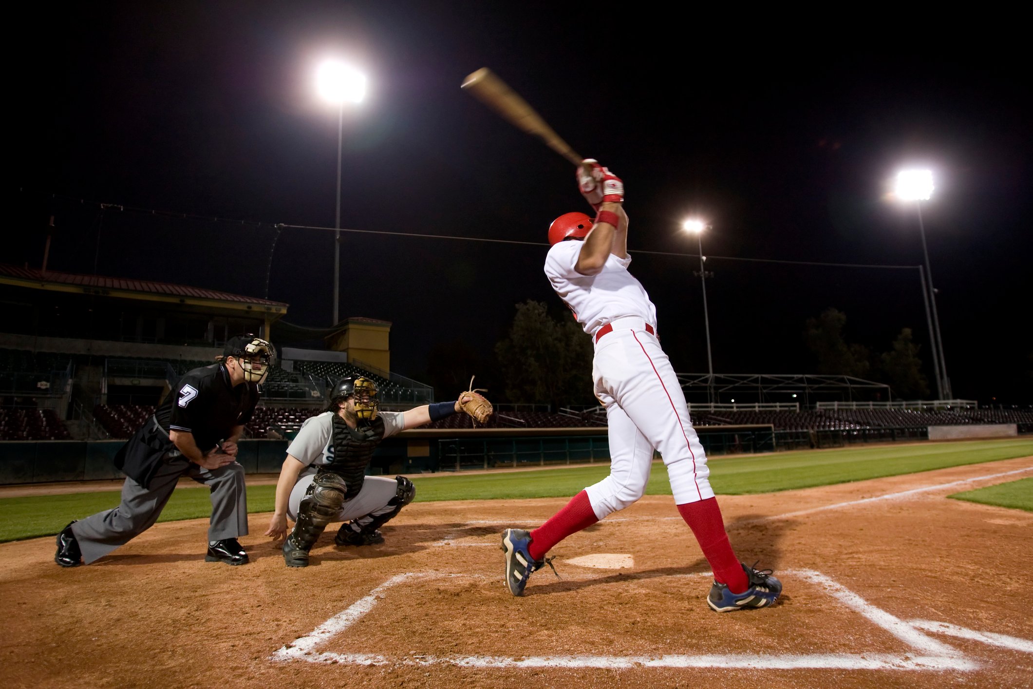 Baseball batter swinging next to catcher and umpire during a night game