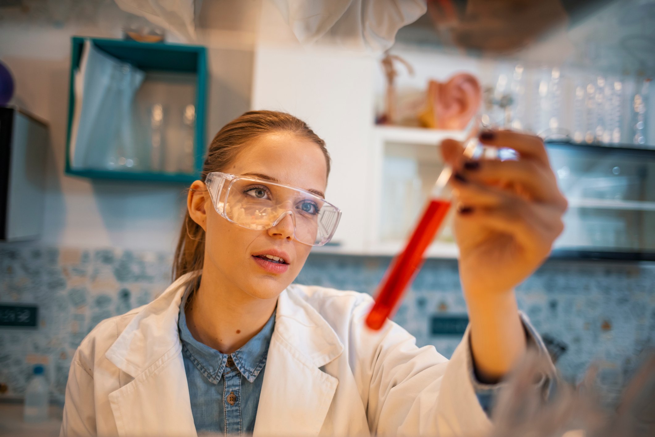A lab worker wearing goggles inspecting a test tube of blood solution.