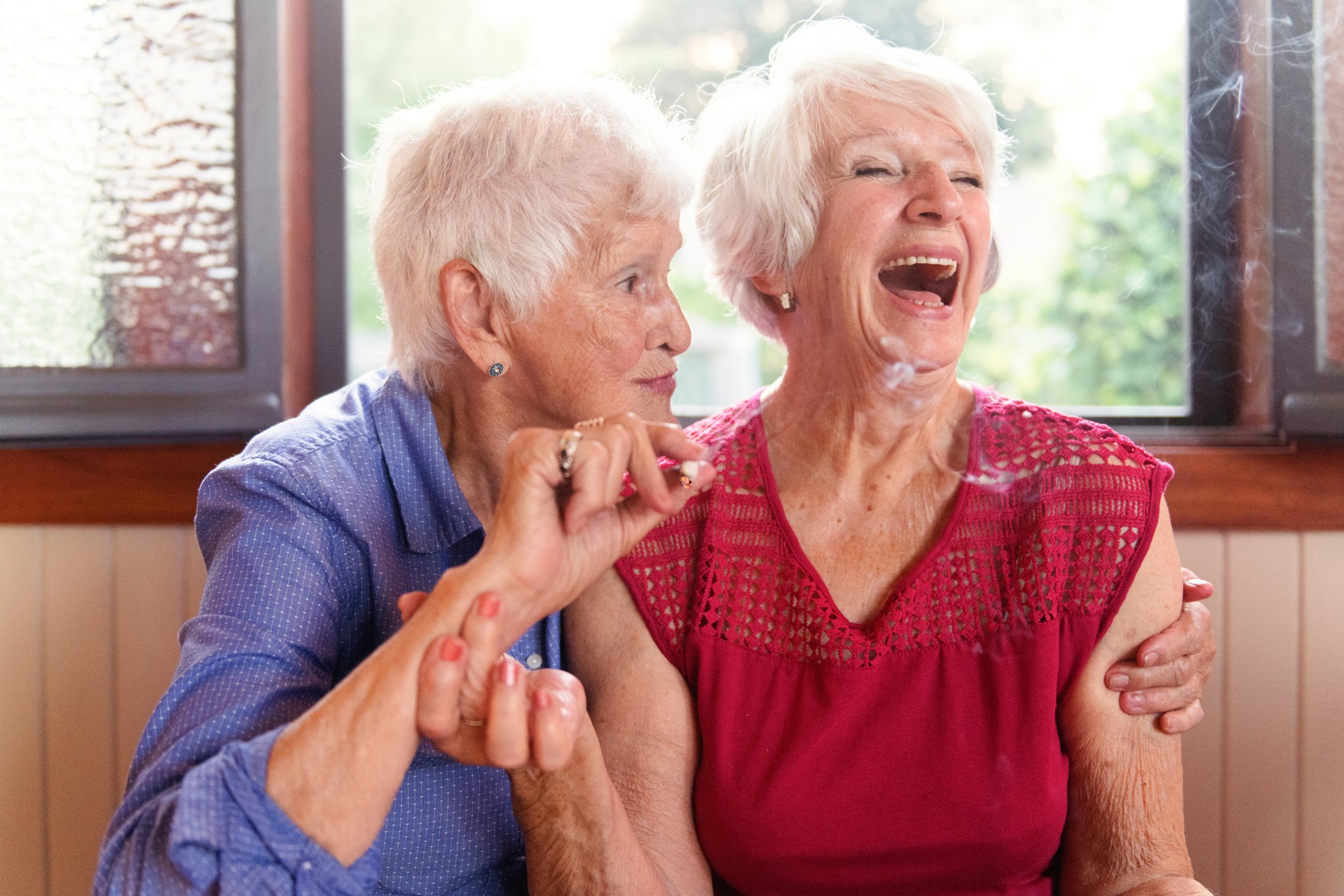 Two elderly women smoking marijuana and laughing.