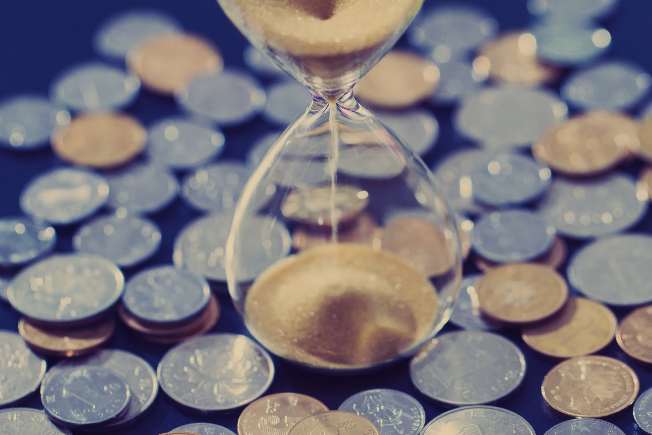 An hourglass stands in the middle of a large pile of coins.