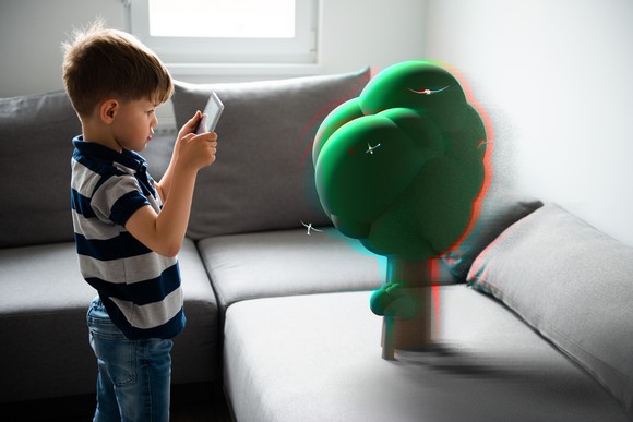 A kid holding up a phone looking at a virtual augmented reality object.