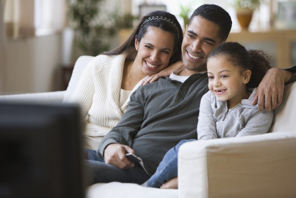 A family sitting on a couch and watching TV.