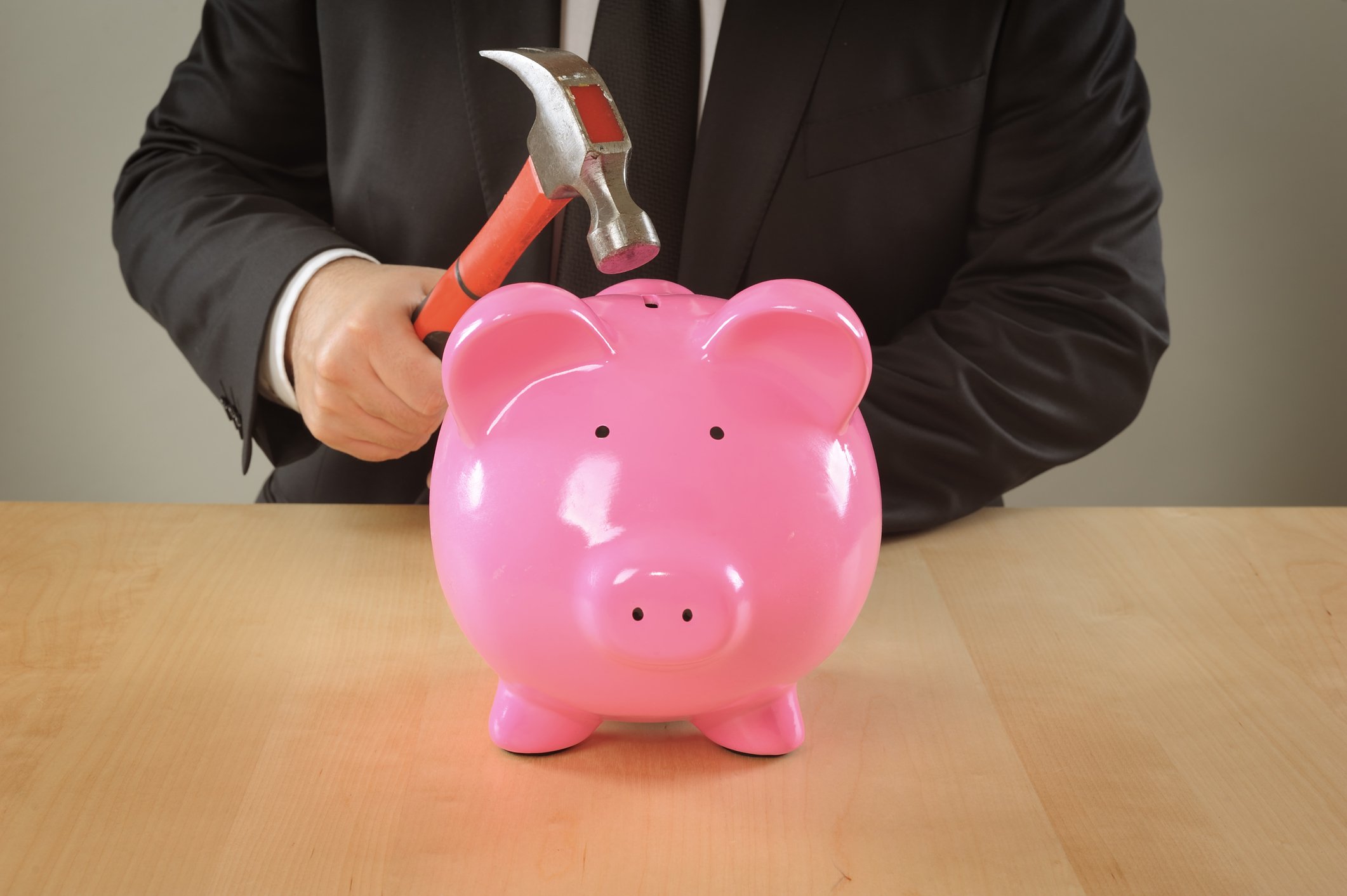 A businessman holds a hammer preparing to break a piggy bank.