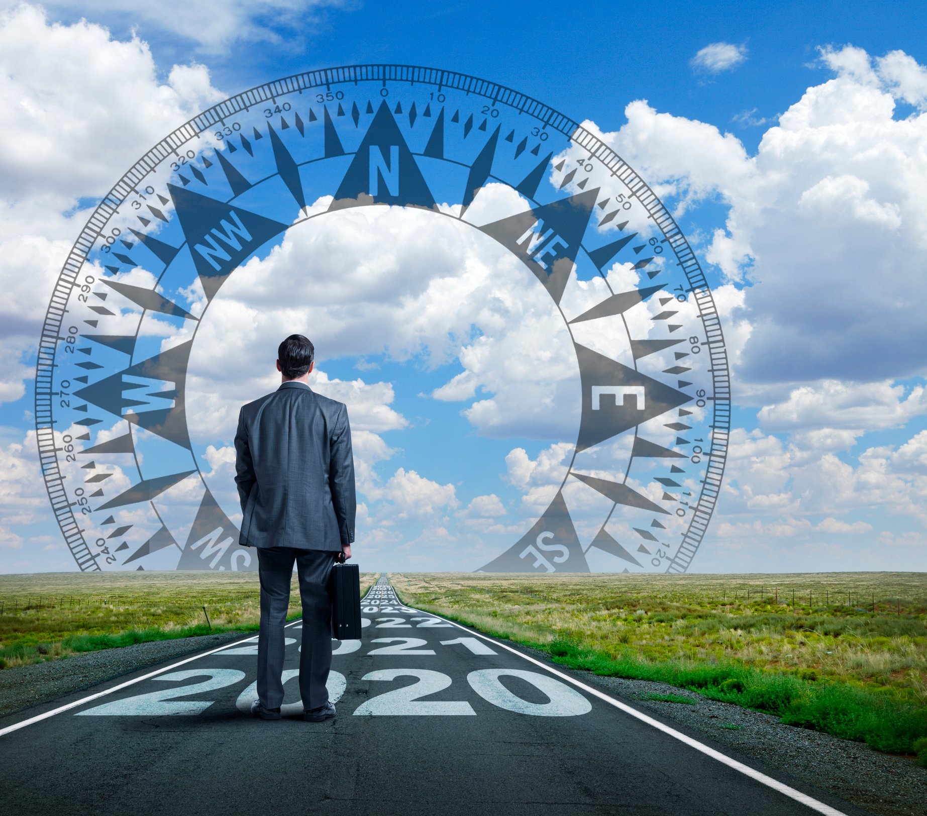 A businessman holding a briefcase looks at a compass in the sky while standing on a road with future years written on it.