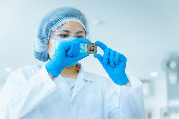 A worker examines a computer chip while wearing safety equipment in a lab setting