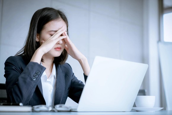 Woman with hands folded in front of her face and a worried look sits in front of an laptop.