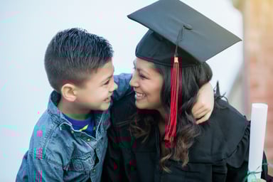 Proud child hugging mom in cap and gown. 