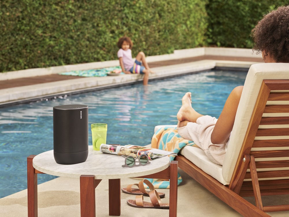 A person sits by a pool listening to a Sonos speaker.