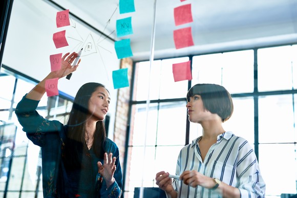 A businesswoman points to a series of sticky notes while talking with a coworker.
