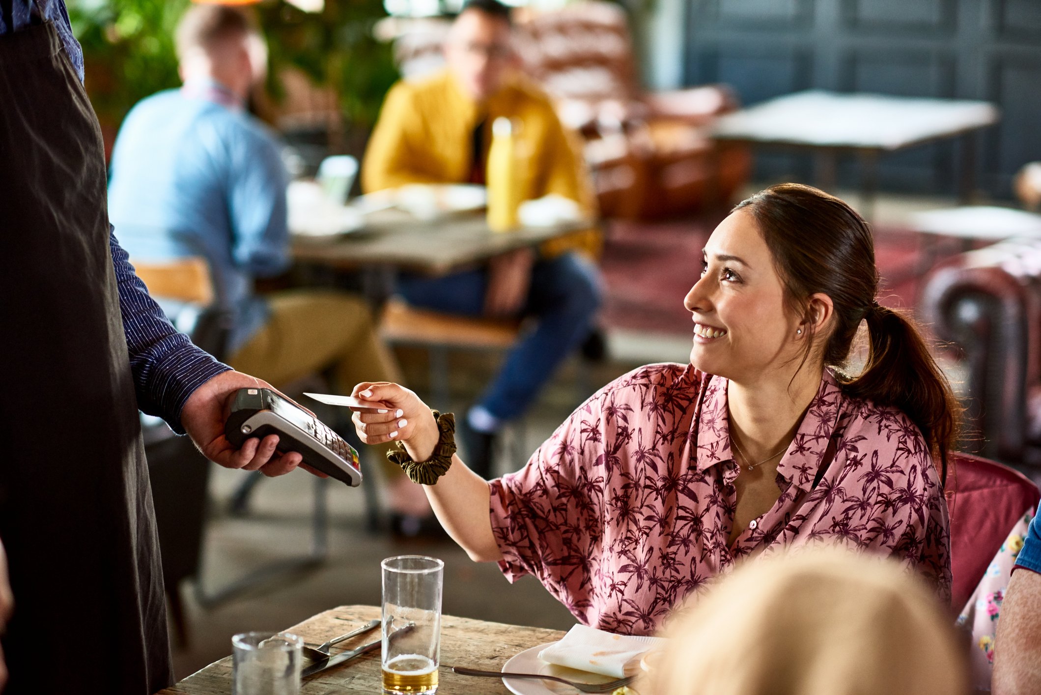 A woman sitting at a restaurant table paying with a credit card.