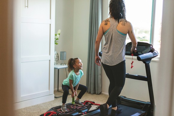 Child looking at lady using treadmill in house.