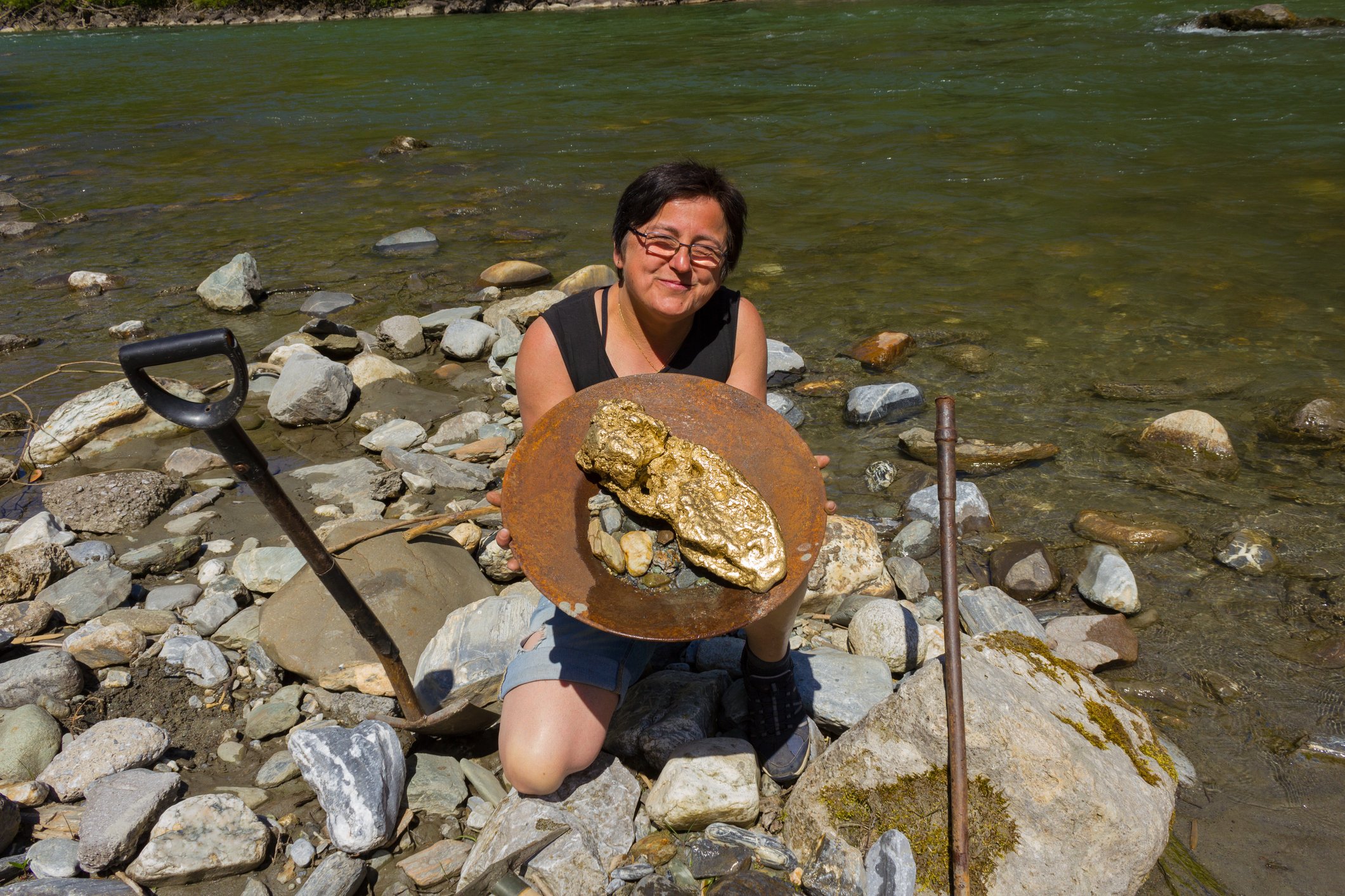 A woman holds up a large pan bearing the gold she's found.