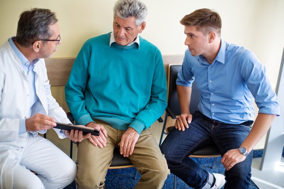 A doctor conferring with one elder and one young man in a healthcare facility.