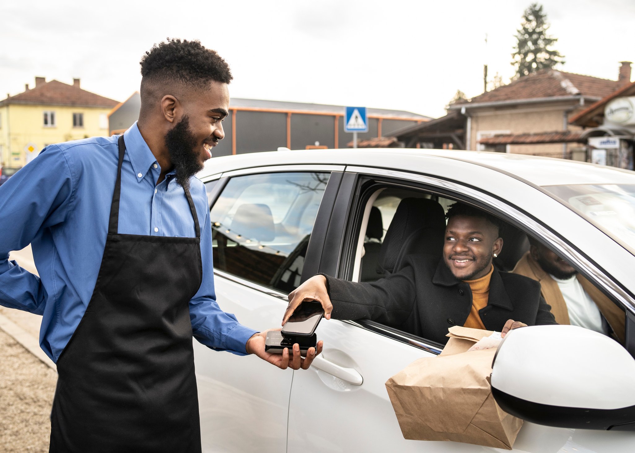 Man in car picking up delivery bag from worker