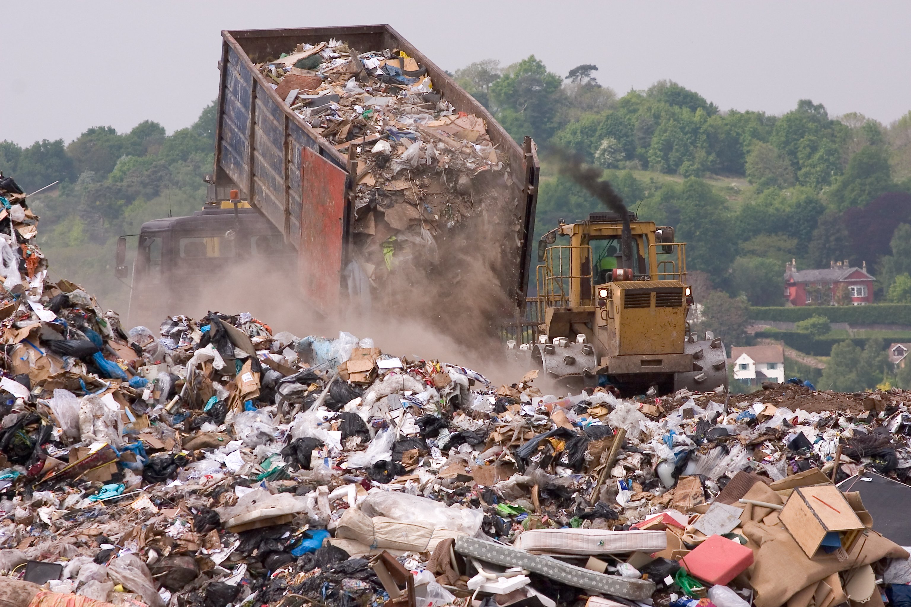 A truck unloads a trailer of garbage at a dump site.