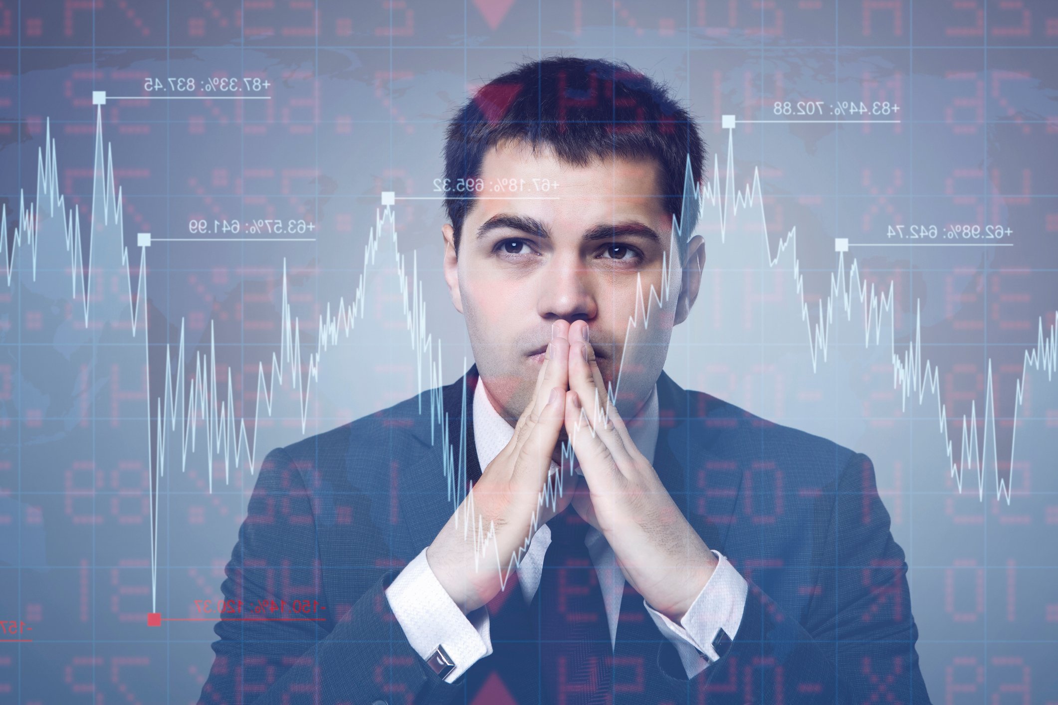 A young man in a suit ponders a fluctuating stock chart superimposed over his face. 