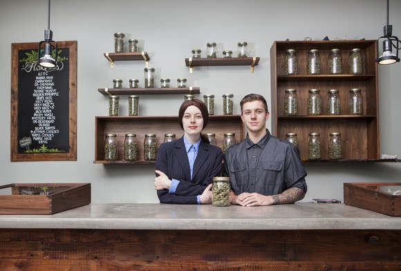 Two people stand at the counter of a marijuana boutique.