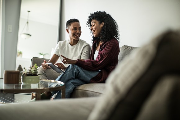 Young couple smiling and sitting on couch looking at tablet