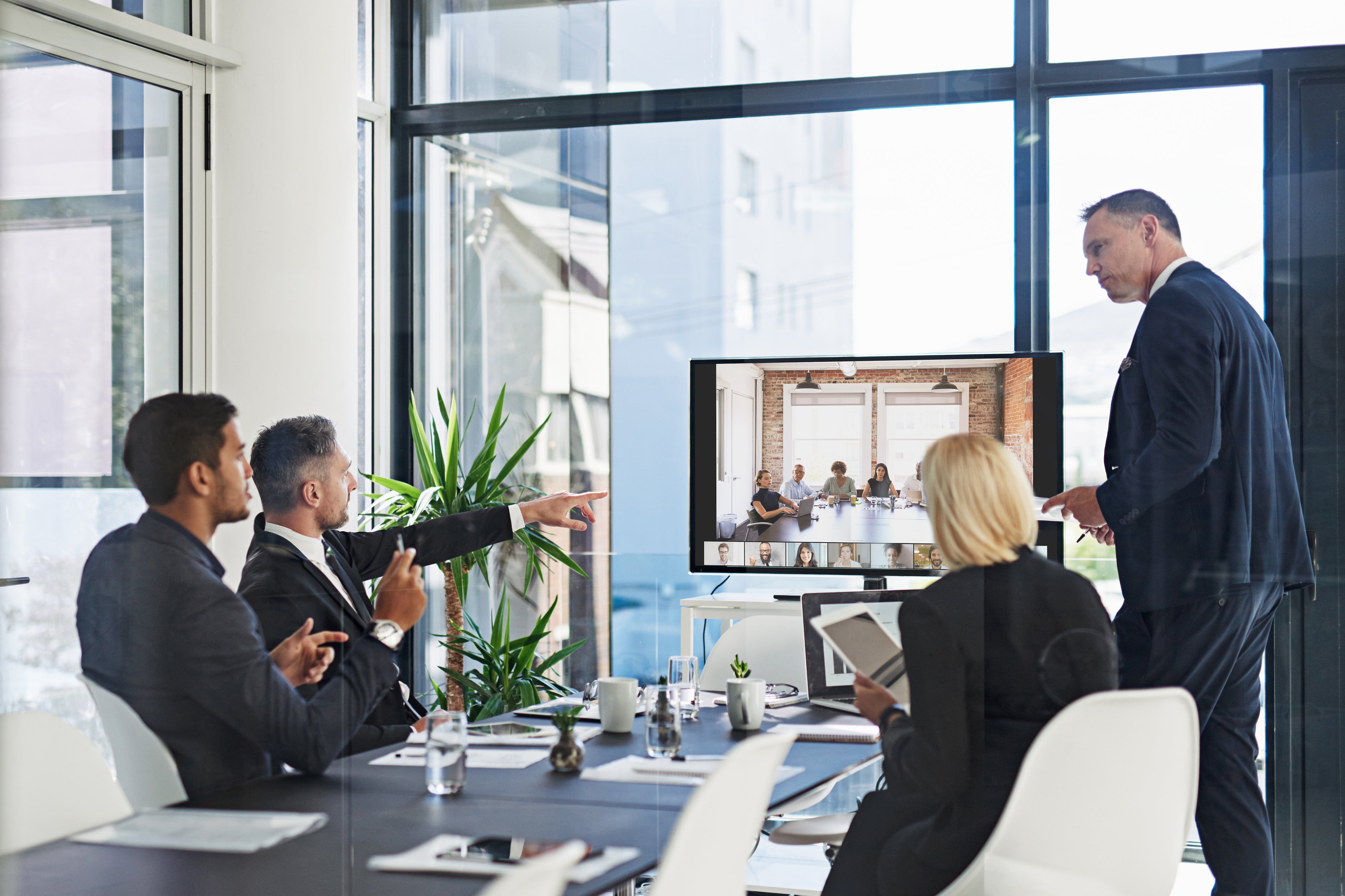 Four employees sit around a conference room table, engaged in a virtual Zoom meeting.