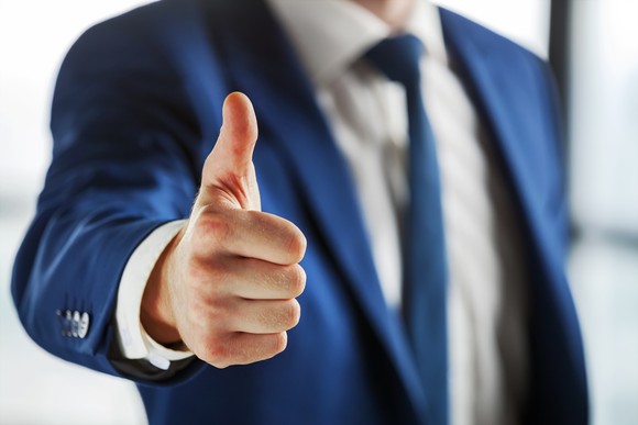 Man wearing coat and tie with thumb up