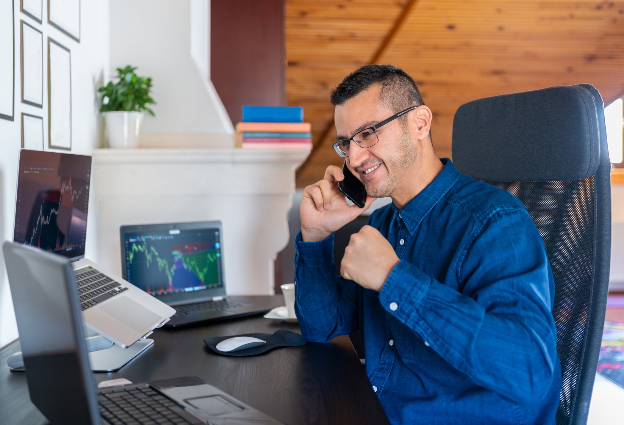 Happy man sitting in front of computer and talking on phone.