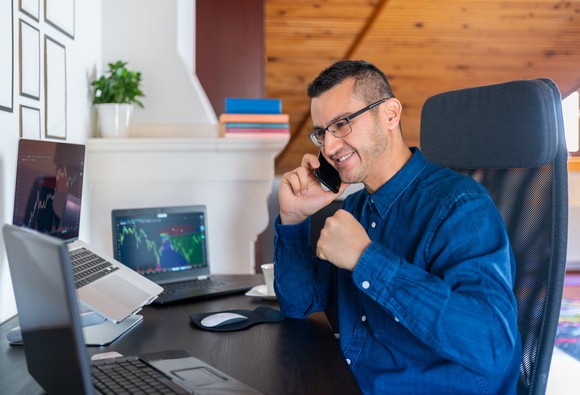 Happy man sitting in front of computer and talking on phone.