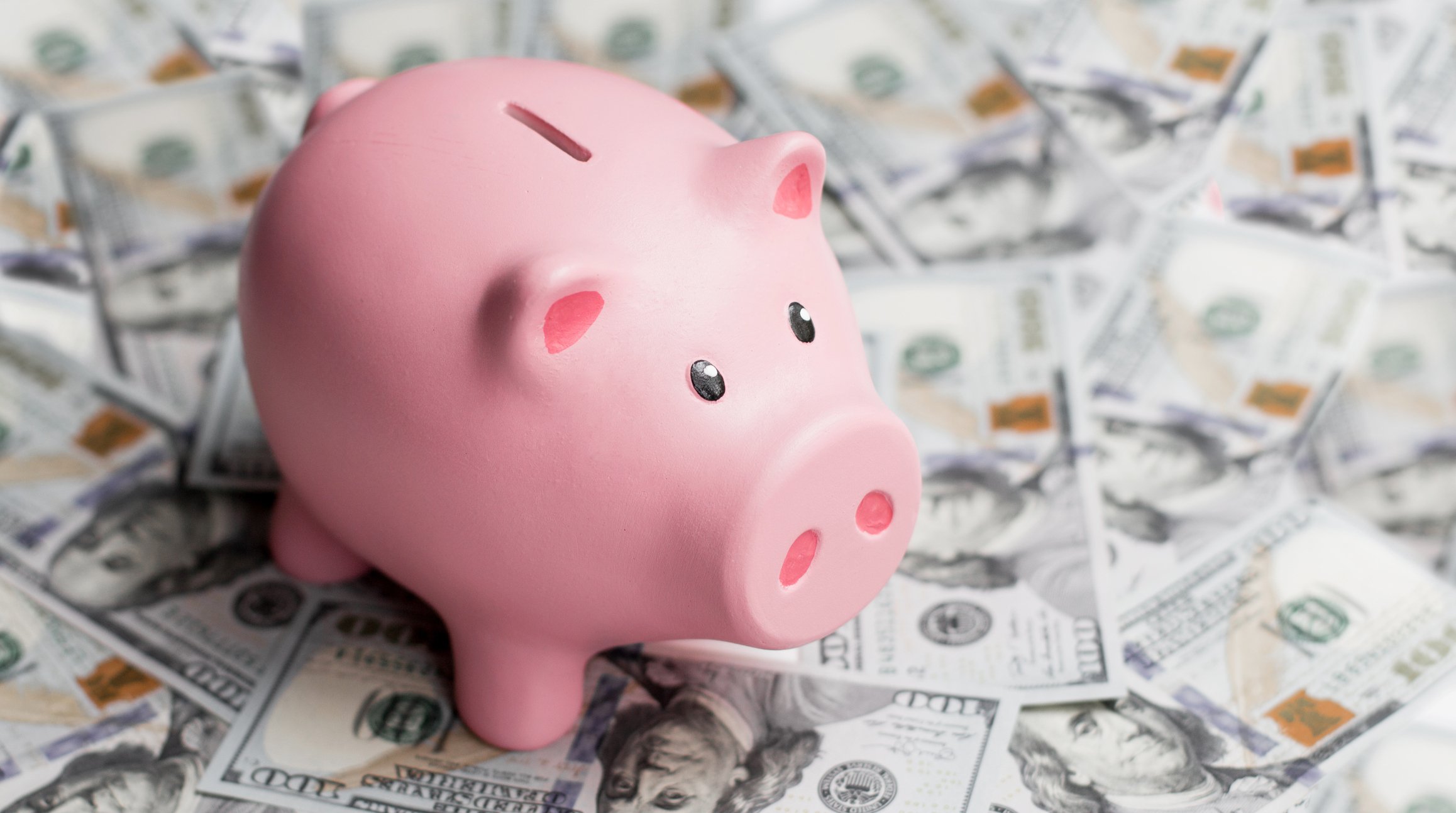 Piggy bank sitting on top of hundred dollar bills.