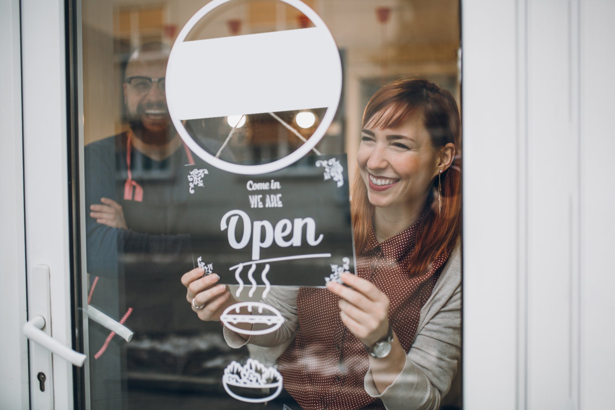 Man and woman with sign saying their store is open.