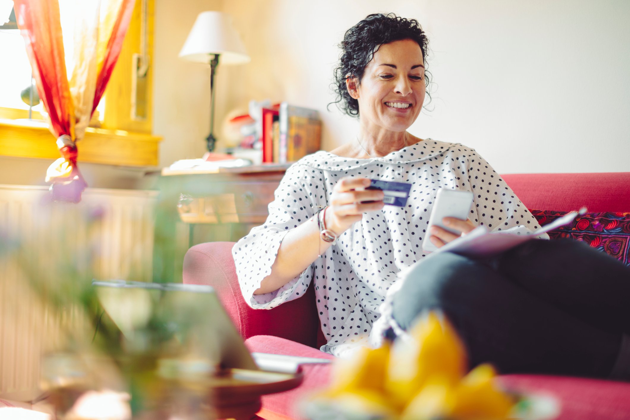 Person sitting on a couch at home and shopping on a cellphone.