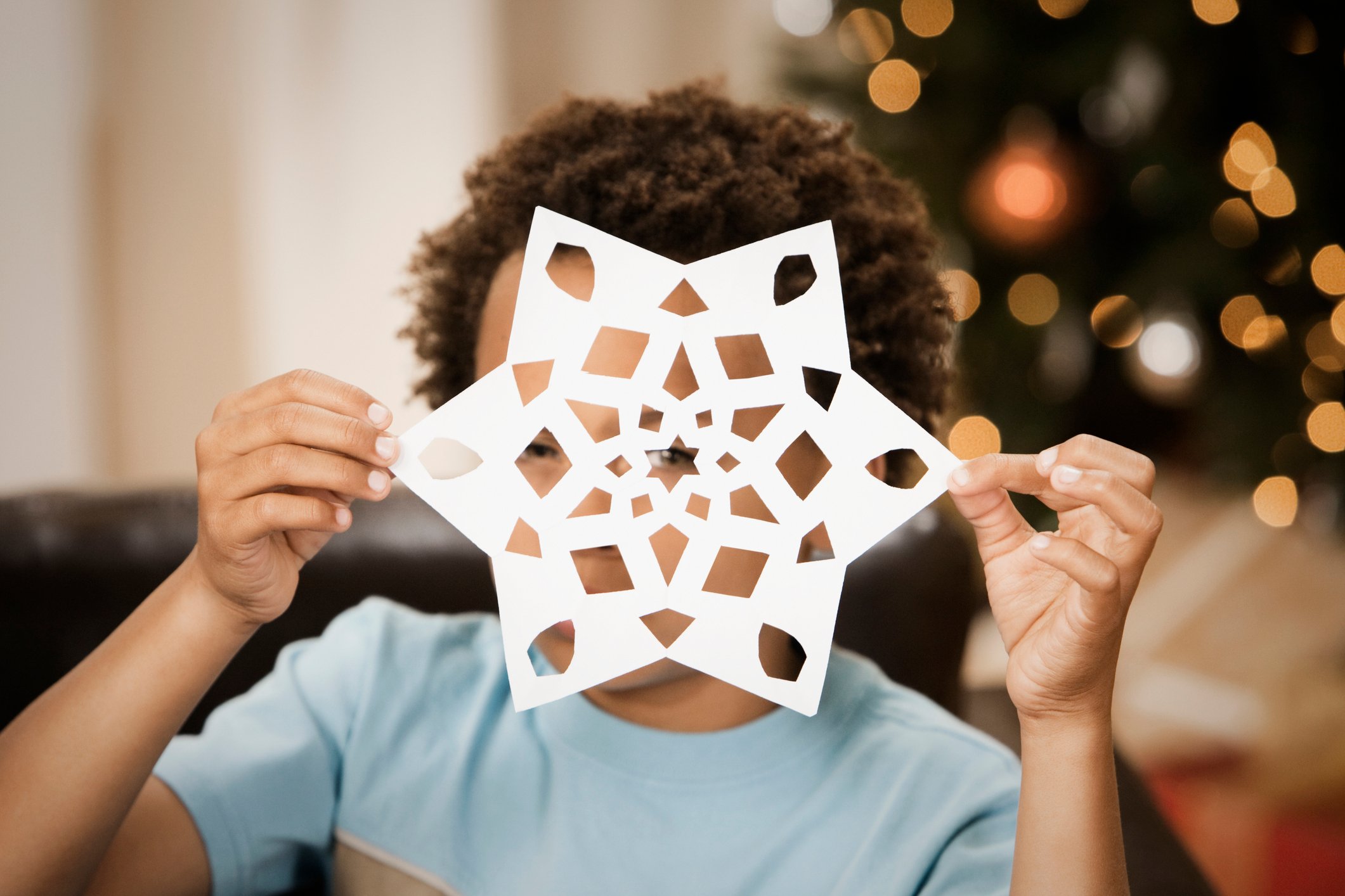 Little boy peering through a paper snowflake.