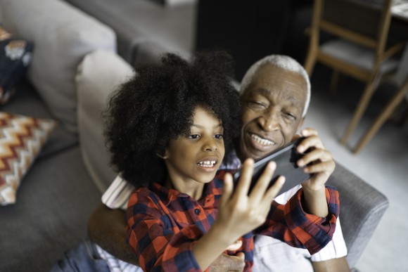A child and their grandparent play a video game on a smartphone together