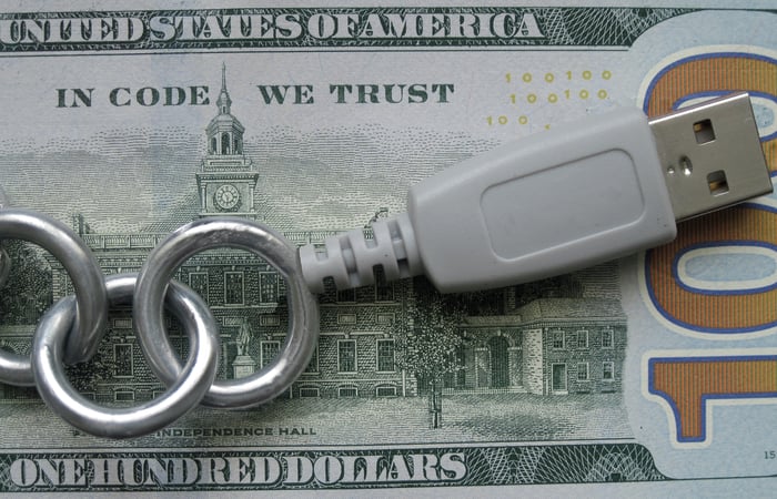 A modified U.S. $100 bill with the words "in code we trust" and a USB drive laying on top of it.